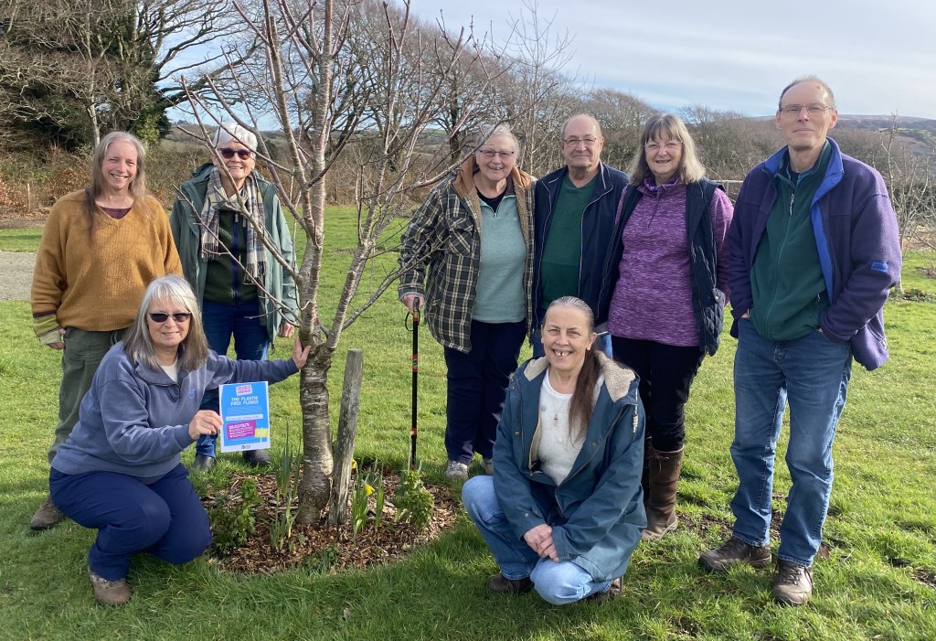 a group of people standing around a tree holding a certificate for the plastic free ally status.